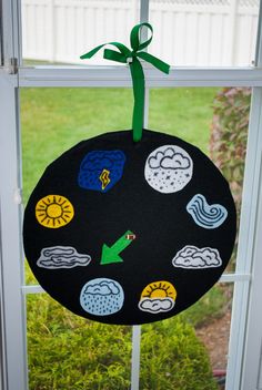 a black round decoration hanging on a window sill in front of a green ribbon