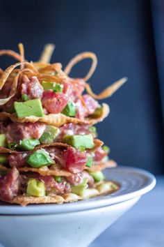 a stack of nachos with bacon, avocado and cheddar