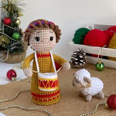 a small crocheted doll standing next to a toy sheep on a table with christmas decorations in the background