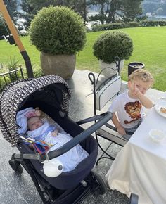 two babies in strollers sitting at an outdoor table