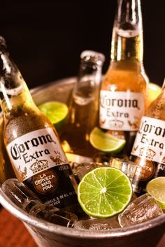 several bottles of corona beer in a bucket with limes and ginger ale on the side