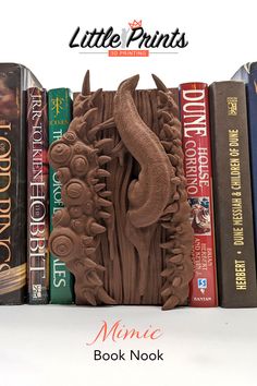 A captivating scene shows the Mimic Book Nook nestled seamlessly among an array of hardcover books on a white background. The 3D printed Mimic Book Nook is designed by Miniatures of Madness, and appears as an ordinary book with intricate details. Its eyes, watchful and curious, peer out from the frame while a mischievous snake-like tongue playfully extends, creating an illusion of life within the mimic's disguise. This whimsical addition adds an element of surprise and fantasy to any bookshelf. Mimic Creature, Fantasy Bookshelf, Mimic Chest, Bookshelf Insert, Tolkien Hobbit, 3d Book, The Mimic, Organize Craft Supplies, Book Enthusiast