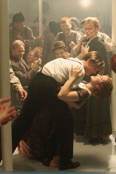 a man and woman kissing in front of a group of people on a subway platform