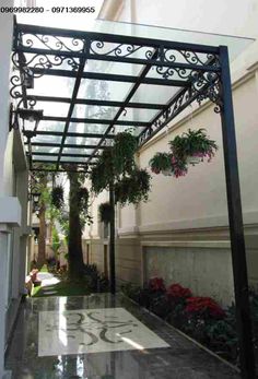 an outdoor covered walkway with plants and potted trees on the sides, in front of a building