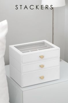 a white dresser sitting on top of a bed next to a lamp with the words stackers above it