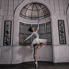 a ballerina is posing in front of an arched window