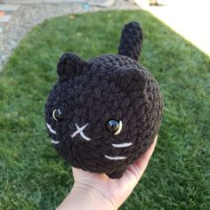 a hand holding a crocheted black cat head on top of some green grass