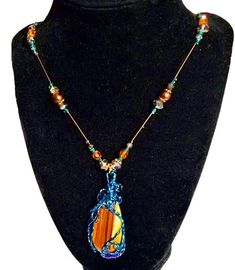 Embrace the grounding and protective energies of Tiger's Eye with this stunning handmade pendant. This unique piece features a polished Tiger's Eye stone, known for its beautiful bands of golden brown and vibrant hues. The stone is intricately wrapped in teal wire, adding an artistic and modern touch to the natural beauty of the gemstone. The pendant is complemented by a meticulously beaded necklace, showcasing a harmonious blend of amber, teal, and clear beads that catch the light beautifully. Each bead is carefully selected to enhance the overall aesthetic, making this necklace a perfect statement piece for any outfit. Tiger's Eye is believed to bring clarity, focus, and confidence to its wearer. Whether you're looking for a meaningful gift or a special addition to your jewelry collectio Bohemian Crystal Necklaces With Natural Stones In Copper, Bohemian Copper Crystal Necklaces With Natural Stones, Brown Jasper Spiritual Jewelry, Bohemian Brown Necklace With Copper Wire, Brown Teardrop Agate Jewelry, Healing Copper Jewelry With Gemstone Beads, Spiritual Brown Gemstone Jewelry, Bohemian Brown Copper Wire Jewelry, Bohemian Brown Copper Wire Necklace