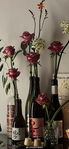 three wine bottles with flowers in them sitting on a table next to two vases