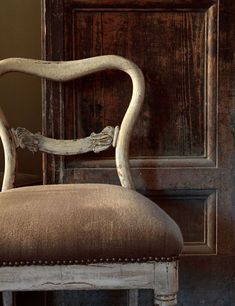 an old chair sitting in front of a wooden door with nails on it's back