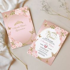 two pink and gold wedding cards on top of a white sheet with flowers in the background