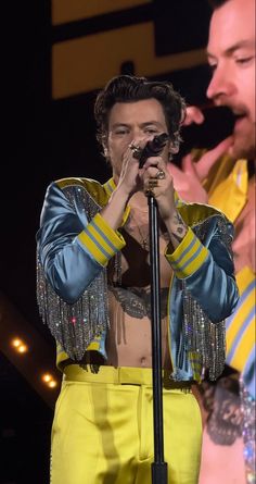 a man in yellow pants holding a microphone and singing into a microphone while standing next to another man