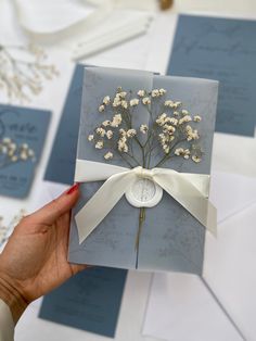 a person holding up a card with flowers on it and white ribbon around the front