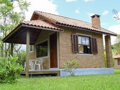 a small brick house with a porch and covered veranda in the grass next to trees