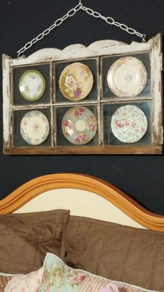 an old window is hung above a bed with plates on it and a chain hanging from the wall