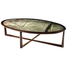 an oval glass table with metal legs and a leaf design on the top, against a white background