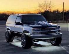 a silver truck parked in a parking lot at sunset with the sun setting behind it