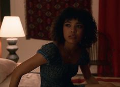 a woman sitting on top of a bed next to a night stand with a lamp