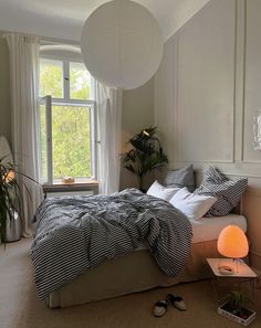 a bed room with a neatly made bed next to a window and a plant on the floor