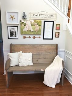 a wooden bench sitting in front of a stairway way with pictures on the wall above it