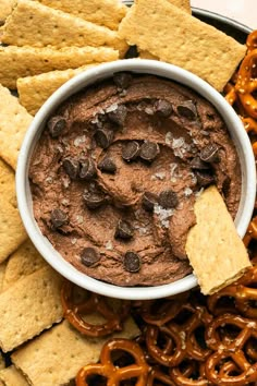 a bowl of chocolate dip surrounded by pretzels and crackers