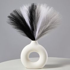 a white vase with black and grey feathers in it on a round table against a gray background