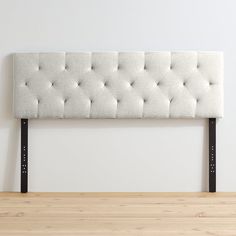 an upholstered headboard with black metal legs and buttons on the top, against a white wall