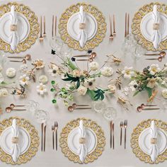 the table is set with white and gold plates, silverware, and floral centerpieces