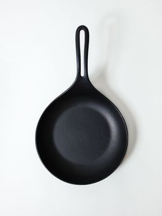 an empty black frying pan on a white surface with the handle extended to the side