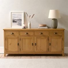 a wooden sideboard with two vases on top of it next to a lamp