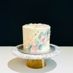 a white and blue cake sitting on top of a wooden stand next to a black wall