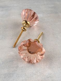 two pink glass knobs on top of a white countertop next to a pair of gold colored handles