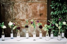 six vases with flowers are lined up on a table in front of a wall