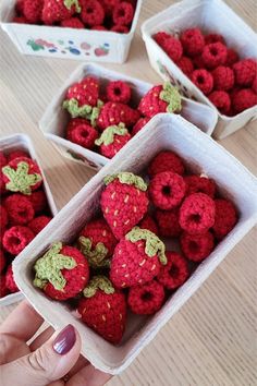 crocheted raspberries in small white containers on a table with one being held up