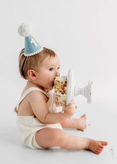 a baby sitting on the floor eating cake wearing a party hat and holding a knife