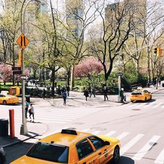 a yellow taxi cab is stopped at an intersection with pedestrians and trees in the background