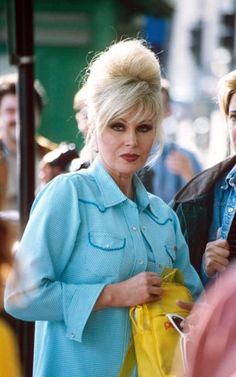 a woman with blonde hair and blue shirt holding a yellow bag while standing next to another woman