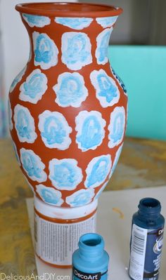 an orange and blue vase sitting on top of a table next to some paint bottles