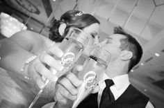 a bride and groom kissing while holding champagne flutes in front of their faces at the wedding reception