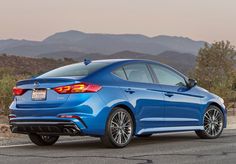 the rear end of a blue car driving on a road with mountains in the background