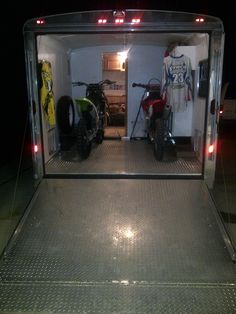 two motorcycles are parked in the back of a trailer with its doors open at night