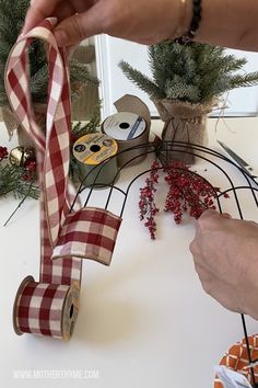 someone is holding a ribbon on top of a wire rack with christmas decorations in the background