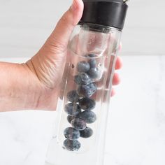 a hand holding a blender filled with blueberries and other fruit in it's container