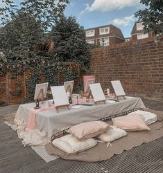 a table with paintings and pillows on it in front of a brick wall, surrounded by trees