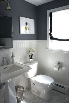 a white toilet sitting next to a sink under a window in a bathroom with gray walls