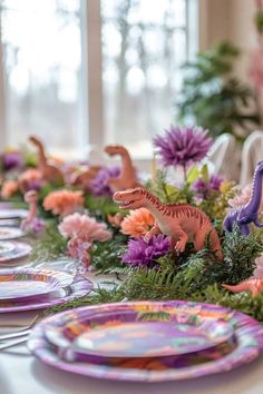 the table is set with plates and dinosaur figurines on top of them, along with flowers