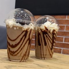 two glasses with ice cream and chocolate swirls on them sitting on a table next to a brick wall