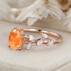 an orange ring sitting on top of a white flowered cloth next to a rose