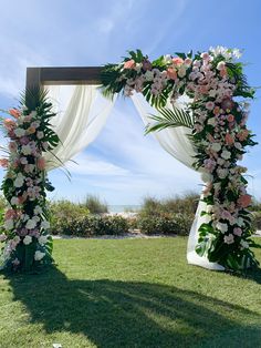 a wedding arch decorated with flowers and greenery on the lawn at an outdoor venue