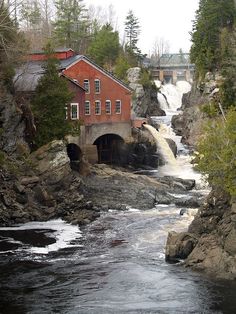 a red building sitting on the side of a river next to a bridge and waterfall